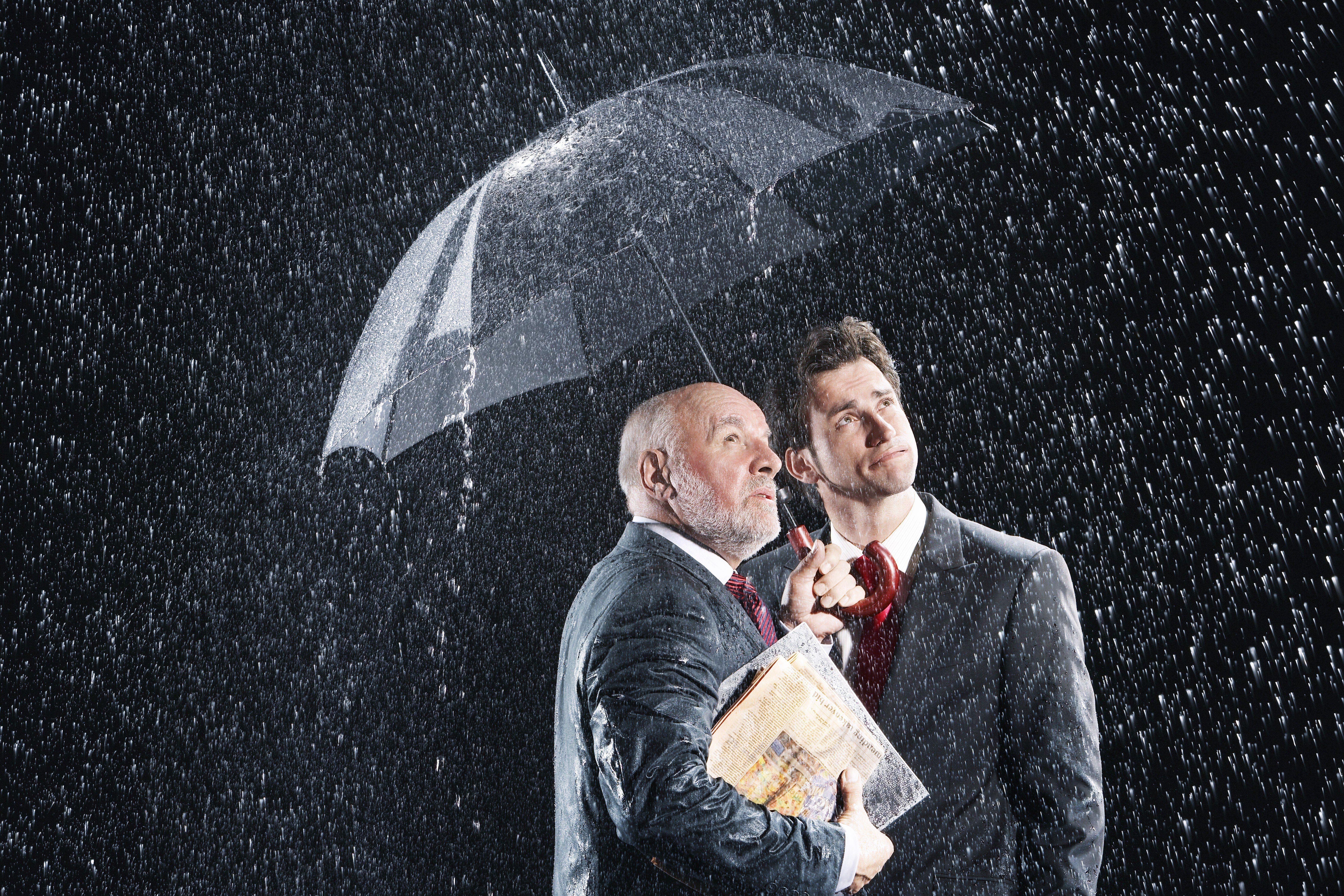Two men in suits standing under an umbrella in the rain and holding file folder