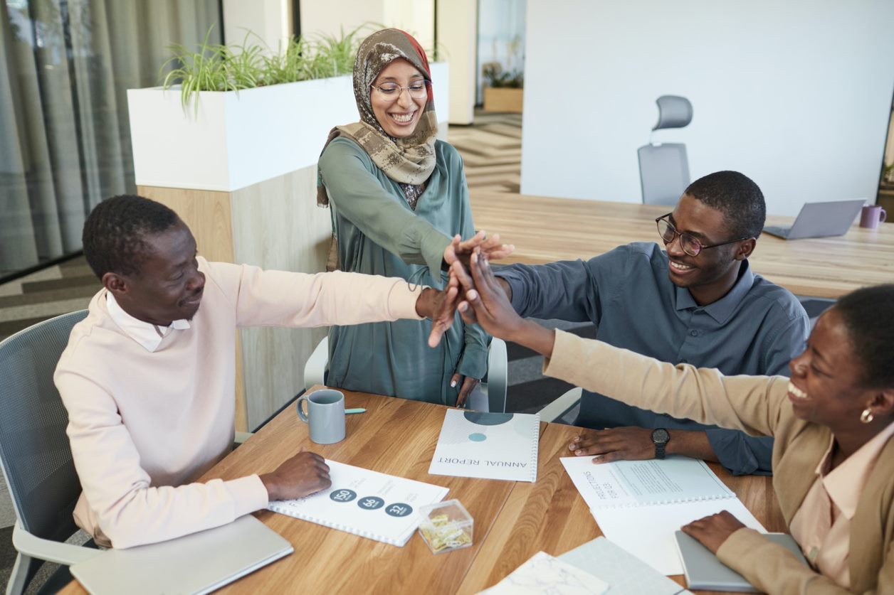 A group of people of varying genders and skin tones high five at a conference table