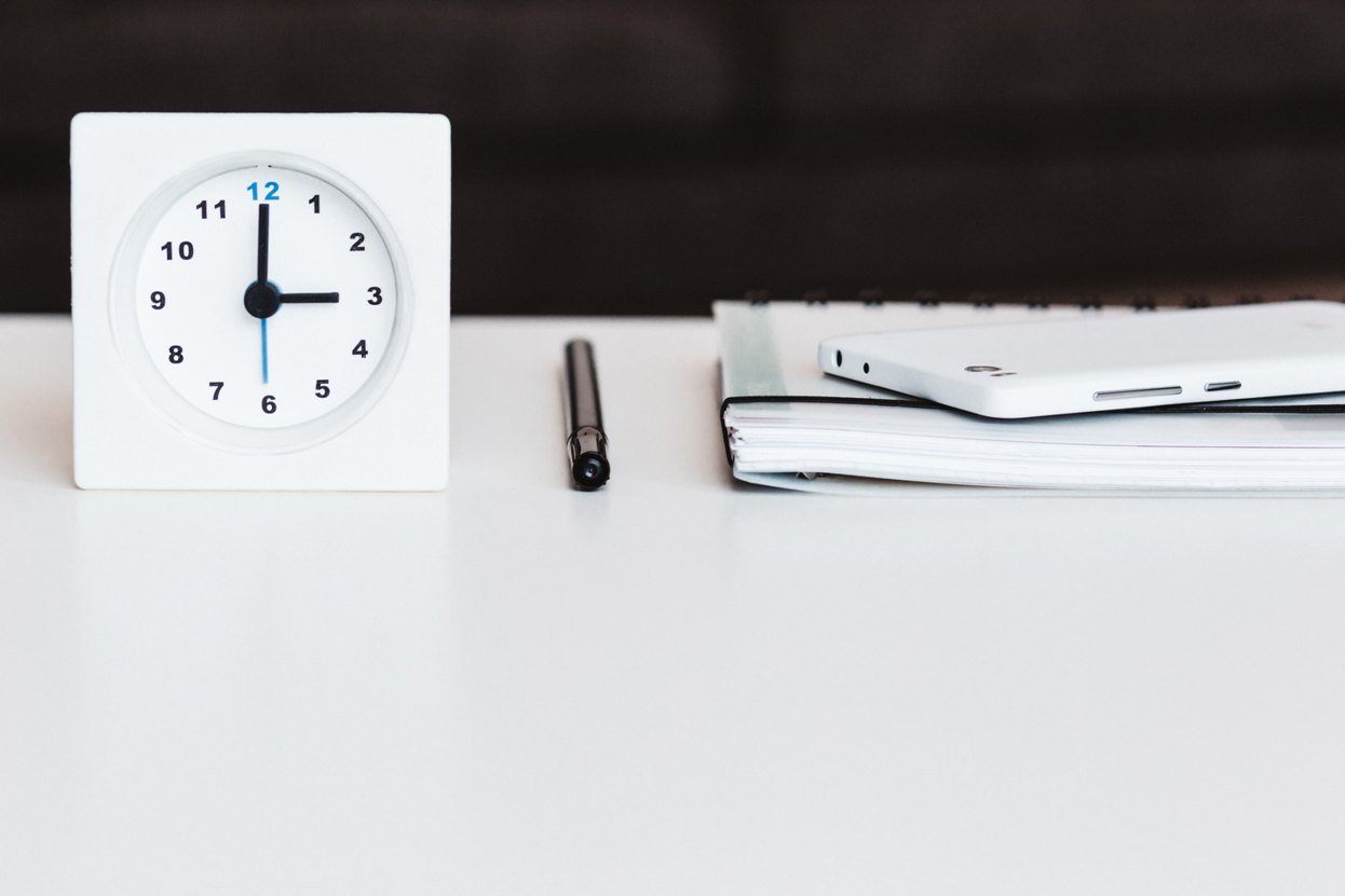 clock, pen, notebook, and phone on a white desk