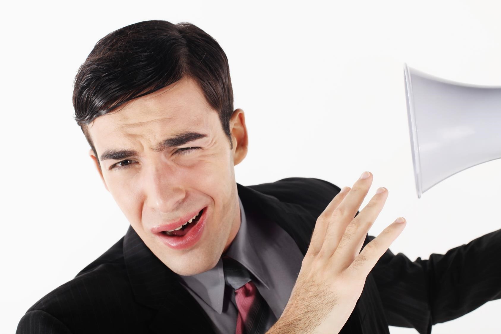 Young white man with dark hair in suit winces with bullhorn at his ear