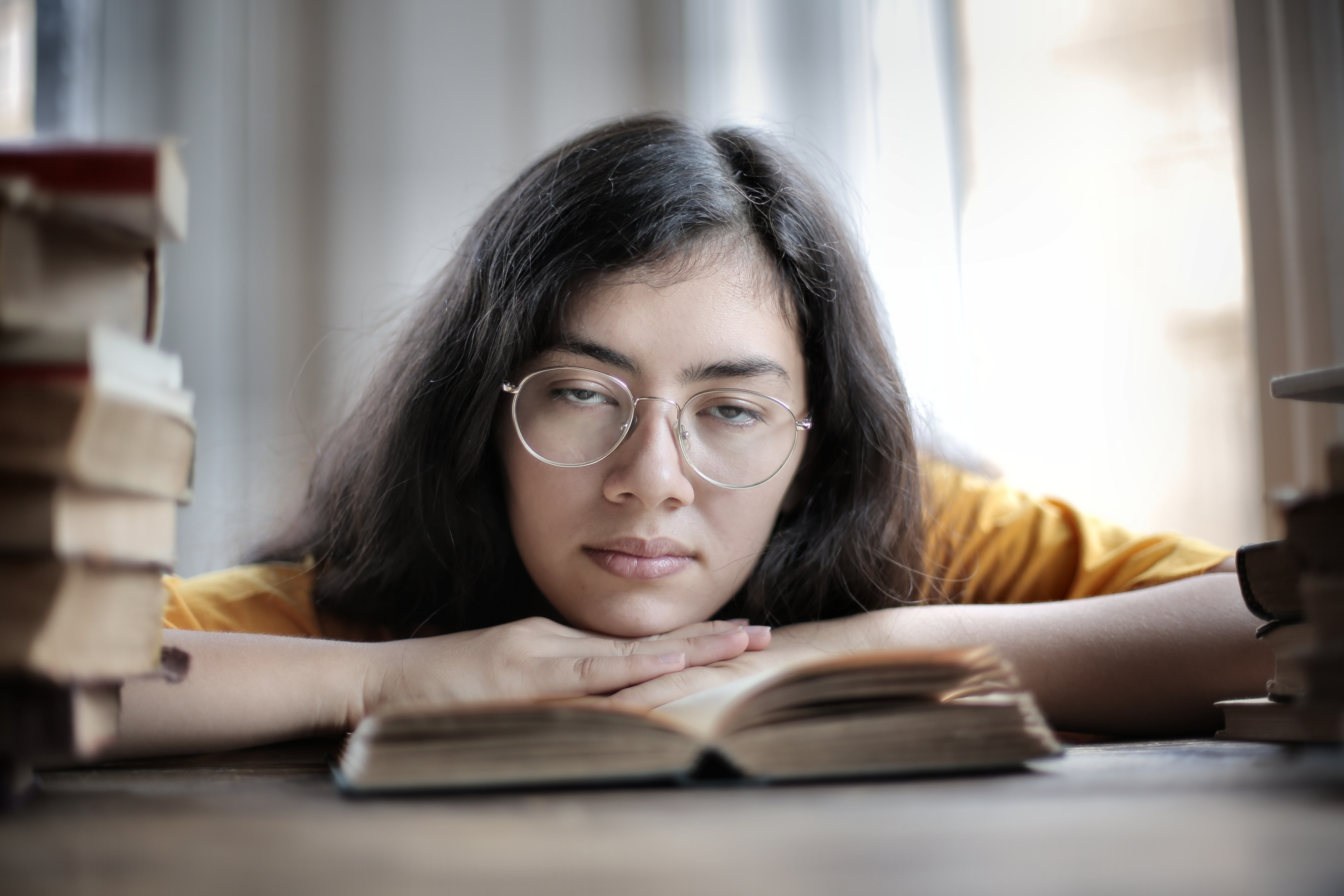 A woman with long hair and glasses dozes off on a book