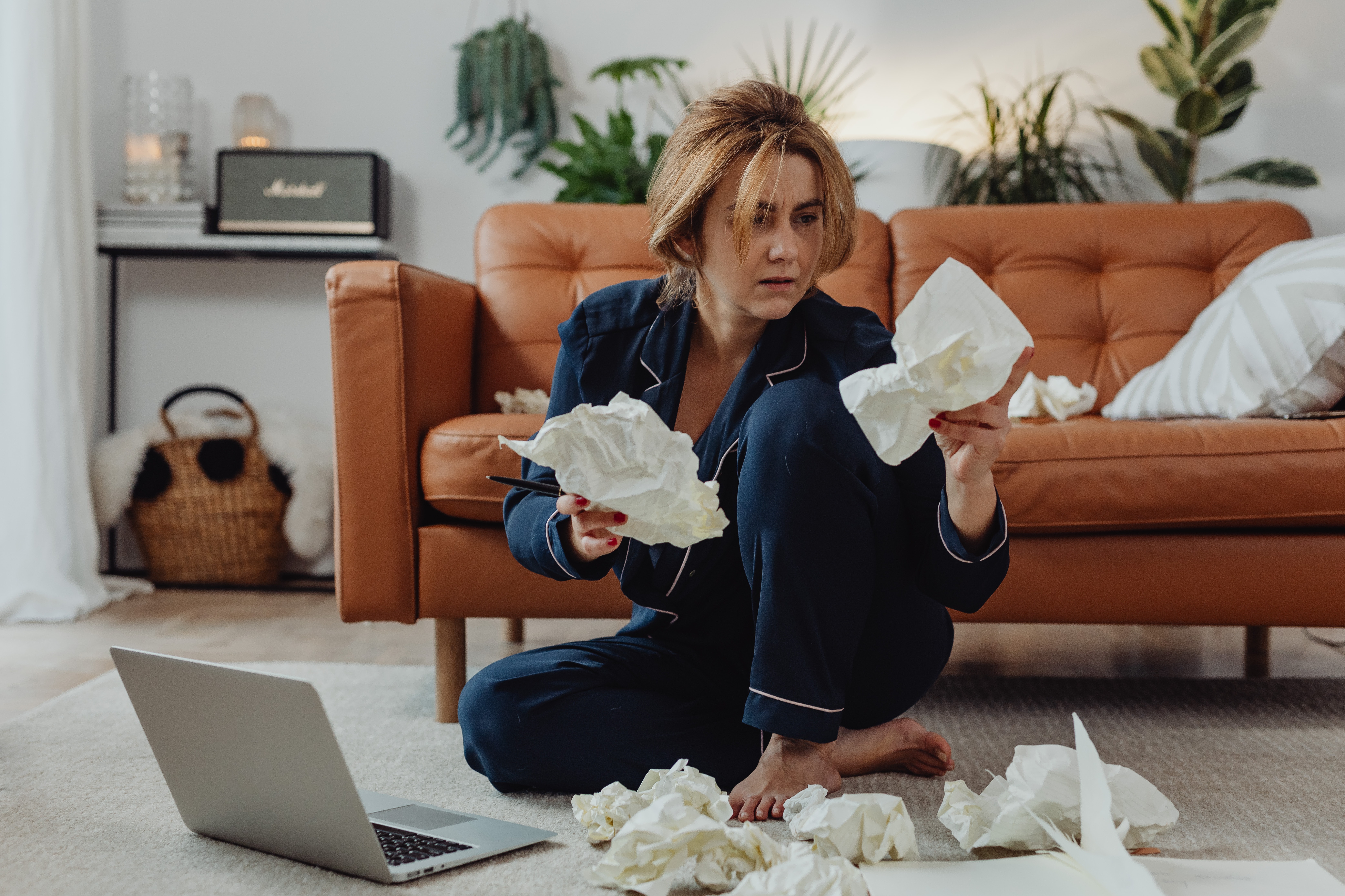frustrated woman with laptop and crumpled paper sitting on floor in front of couch